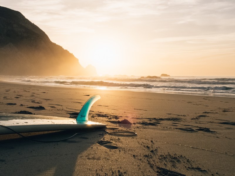 an abandoned surfboard upside down left on the beach as the sun sets over the sea in the background, surfboard at sunset 4k