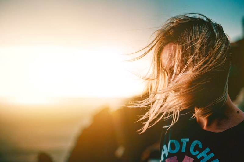 a woman with windswept hair in front of rocks water and sunshine in lubenice, summer 4k