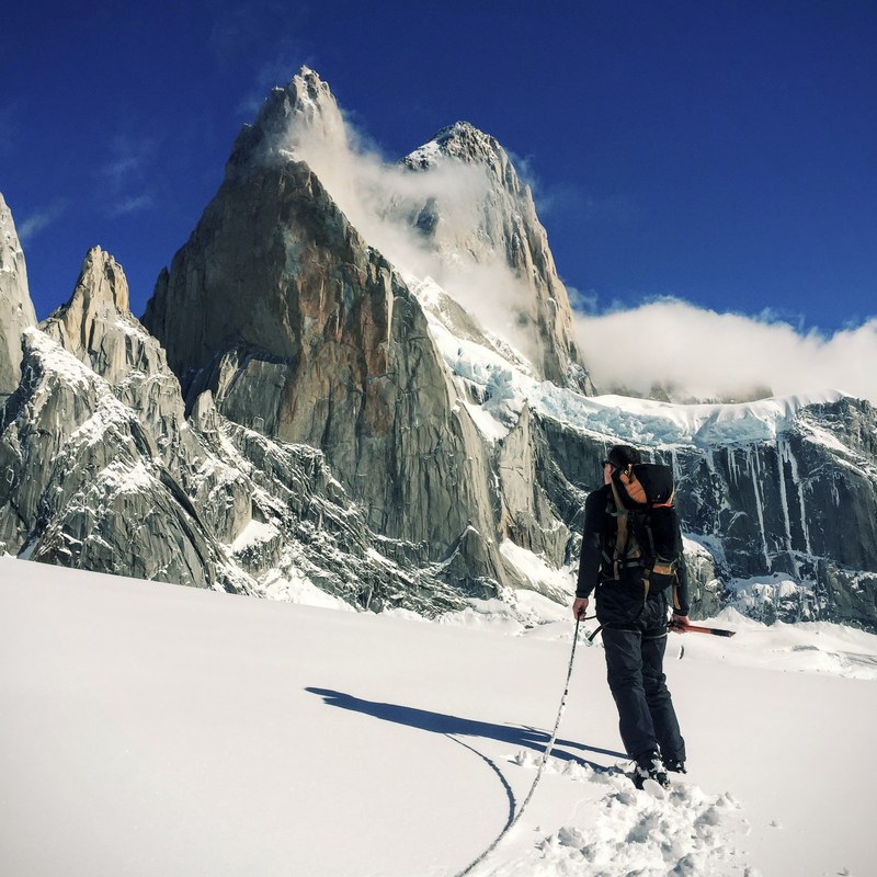 a man with mountaineering gear looks at a steep jagged peak on a snowy day, preparing to ascend the peak 4k