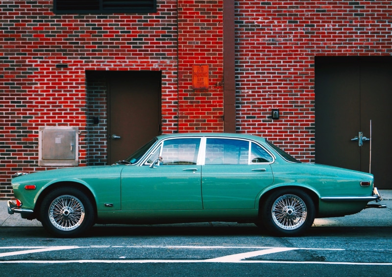 chrome, headlight, coupe, city, motor vehicle, auto, driver, built structure, brick wall, outdoors, mode of transportation, transportation system, day