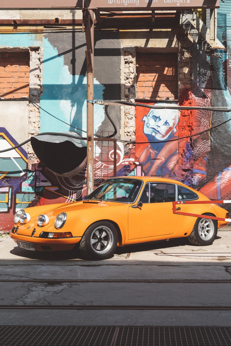 machine, porsche, city street, parked, spoke, 8K, taxi, billboard, outdoors, graffiti, street, built structure, transportation, sunlight, tire, nature