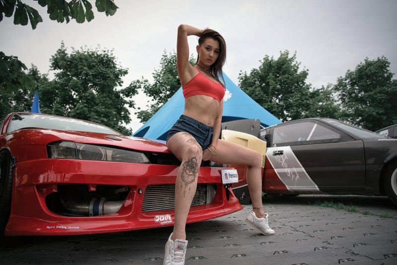 hairstyle, tree, portrait, women, pierced navel, looking at camera, car, beautiful woman, jean shorts, land vehicle, clothing, lifestyles, women outdoors