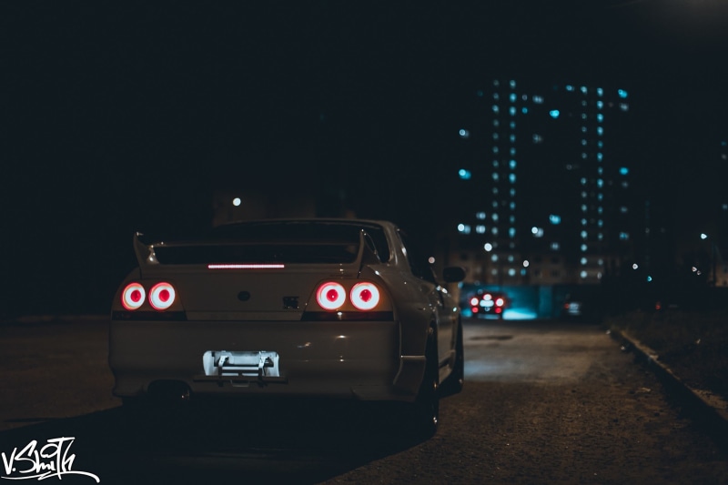 street, sedan, building exterior, motor vehicle, road, car, night, white, architecture, red, lights, built structure, lighting equipment, no people, transportation