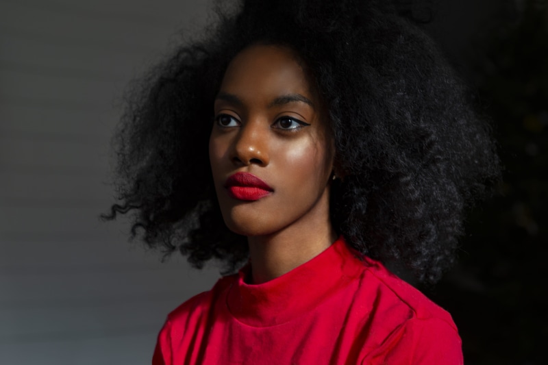 hairstyle, person, hair, indoors, young woman, red, studio shot, lips, turtleneck, top, young adult, beautiful woman, sideways, close-up, focus, black background