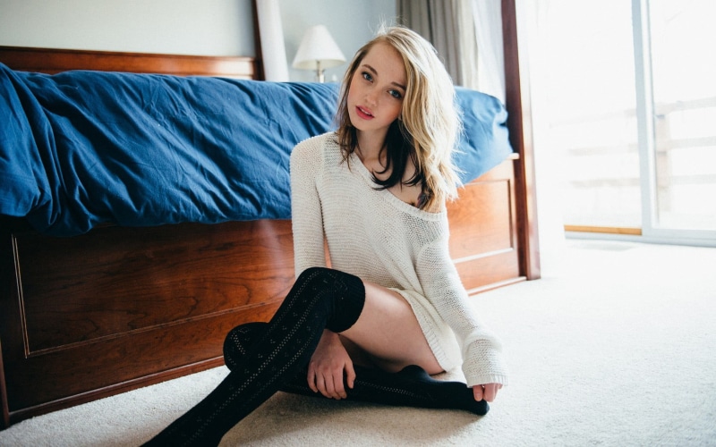 looking at viewer, hairstyle, blond hair, blonde, bedroom, sitting, Jillian West, top, beautiful woman, casual clothing, contemplation, blue eyes, indoors