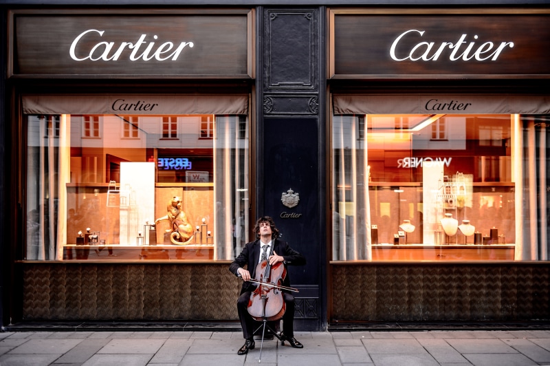 storefront, standing, building exterior, cartier, casual clothing, footpath, window, full length, cello, city, sidewalk, man, outdoors, street, shop, shopfront