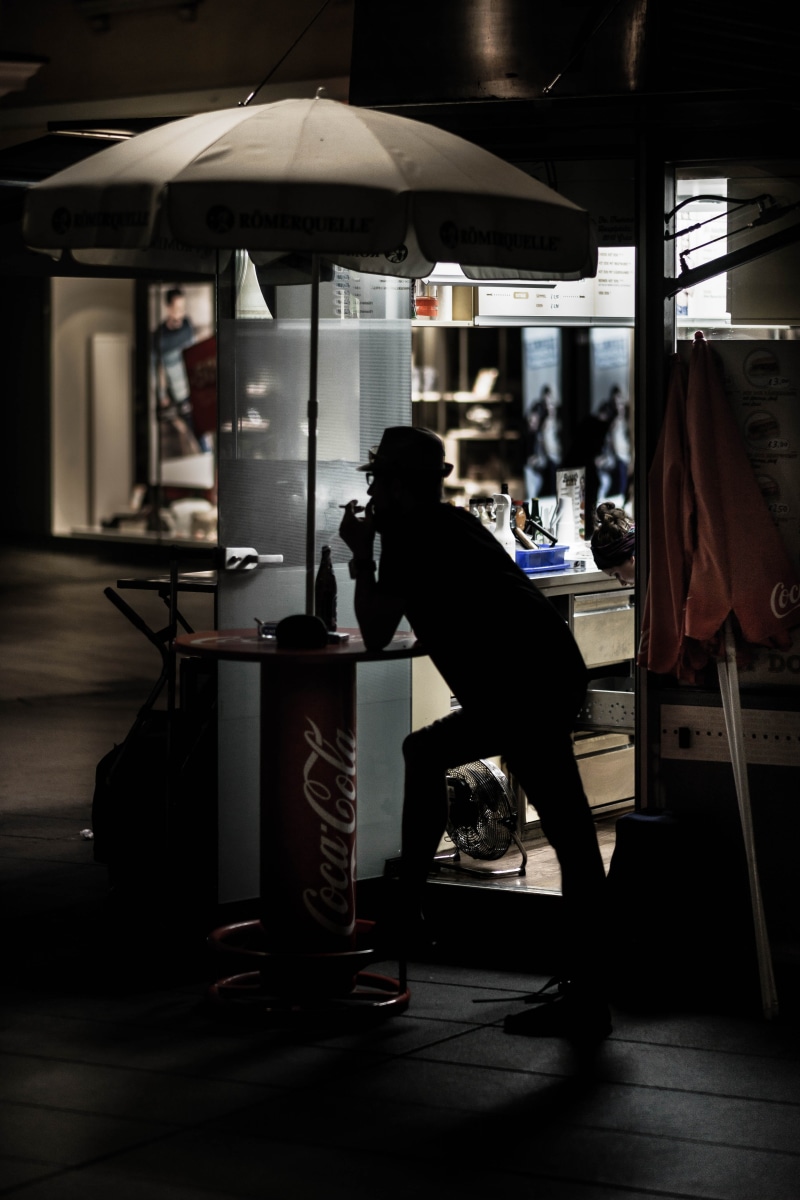 street, leaning, urban, real people, silhouette, leisure activity, men, adult, lifestyles, day, storefront, bending, city, table, full length, side view