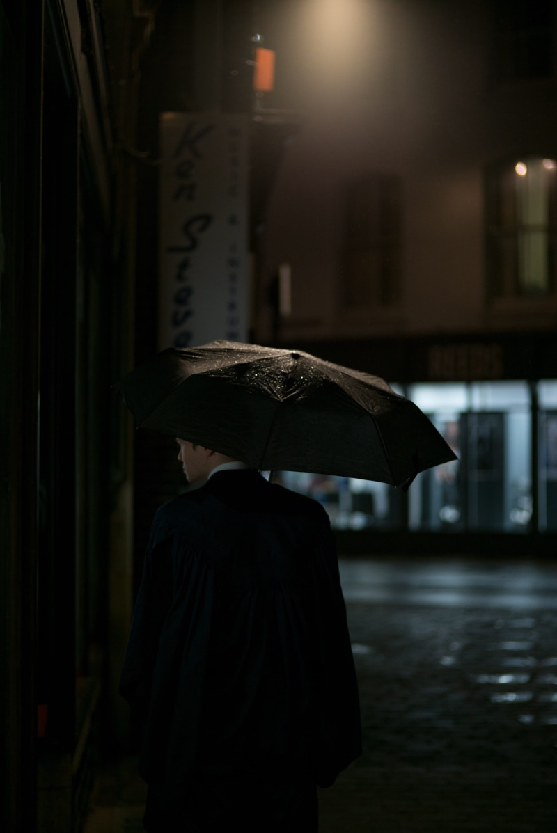 standing, umbrella, wet, building exterior, dark, 5K, clothing, focus on foreground, male, city, built structure, rainy season, jacket, black, men, lifestyles