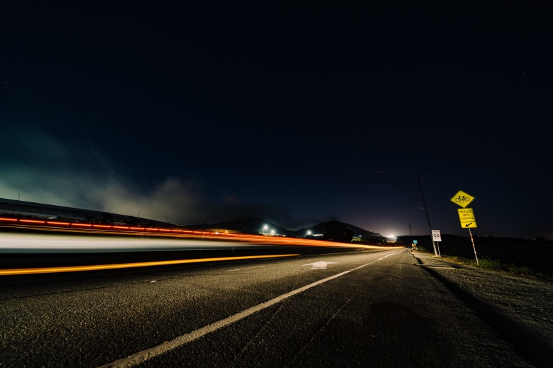 vehicle light, traffic, light trail, direction, black, blurred motion, street, street sign, city, speed, mode of transportation, photo, neon lights, fog