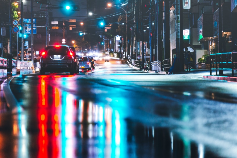 rain, building exterior, nightlife, city life, building, beside, surface level, water, cityscape, city, traffic, architecture, motion, urban, wet, vehicle