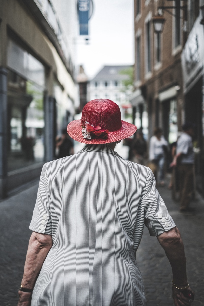 city, focus on foreground, alley, wearing, city life, back, women, real people, redhat, outdoors, sun, waist up, clothing, person, old woman, urban, day