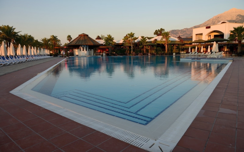 outdoors, water, tranquil scene, poolside, tourist resort, building, pool, tiled floor, reflection, tropical climate, hotel, swimming pool, parasol, nature