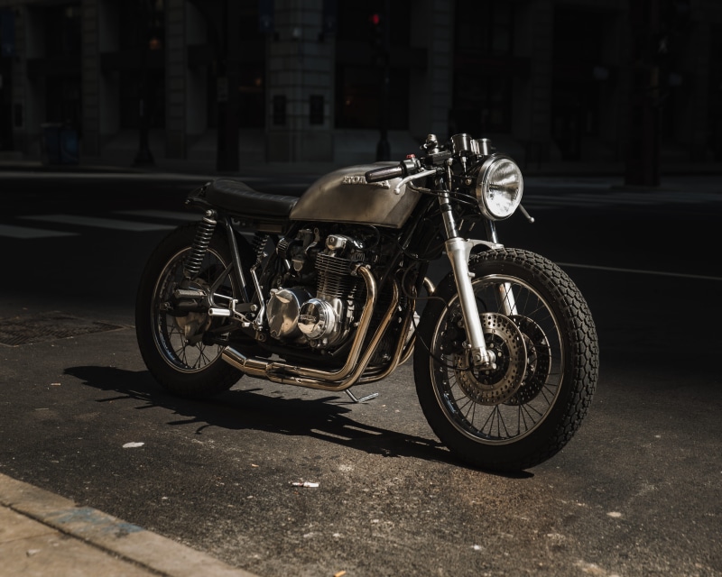 building exterior, transportation, road, wheel, focus on foreground, 4K, street, land vehicle, no people, cafe racer, motorcycle, stationary, sunlight