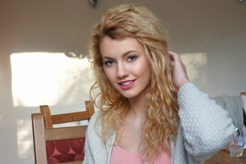 sweater, pink lipstick, curly hair, open mouth, smiling, blonde, brown eyes, portrait, model, 1080P, looking at viewer, women indoors, white sweater, pink tops