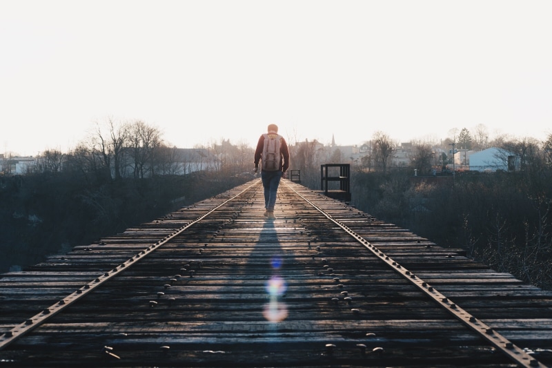architecture, diminishing perspective, standing, adult, track, walking, direction, rear view, bridge, sunlight, backpack, along, full length, rail transportation