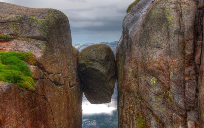 tranquil scene, cliff, focus on foreground, close-up, non-urban scene, mist, mountains, grass, nature, solid, outdoors, rock - object, day, cloud - sky