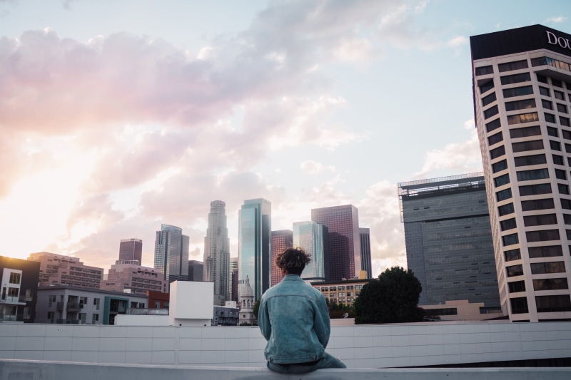 real people, person, skyscraper, buildings, building exterior, office building, town, apartment building, standing, man, sitting, ledge, downtown, apparel