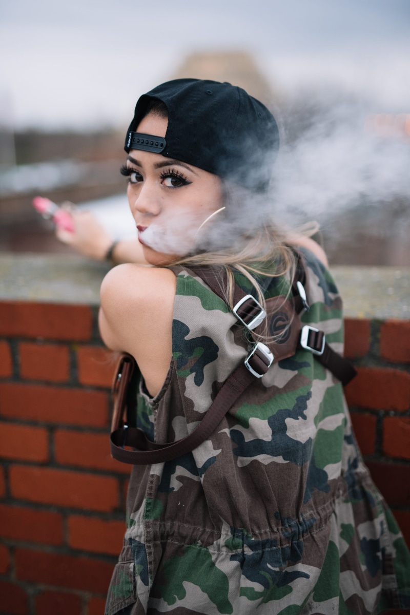vaping girl, looking at camera, government, young adult, wall, waist up, outdoors, vaping, one person, focus on foreground, front view, 2K, beautiful woman