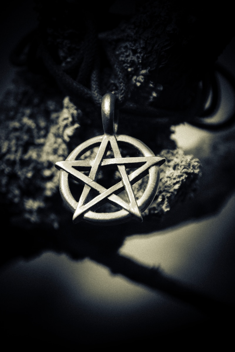necklace, witchcraft, 5K, plant, black, black background, witch, scary, indoors, focus on foreground, pendant, field, pentagram, symbol, selective focus