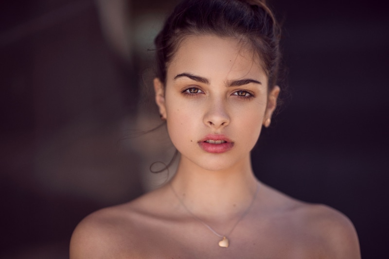 looking at viewer, brunette, depth of field, model, bokeh, necklace, brown eyes, 1080P, face, portrait, pink lipstick, bare shoulders, women