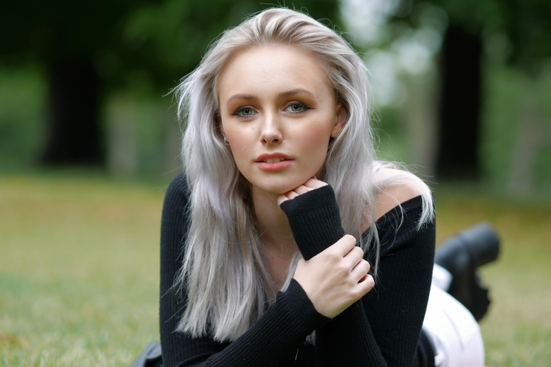 lying on front, portrait, women, black tops, looking at viewer, 1080P, pants, women outdoors, touching face, outdoors, trees, gray eyes, depth of field