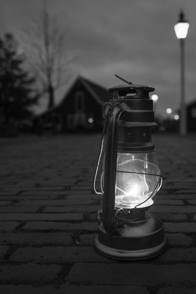 building exterior, oil lamp, cobblestone, architecture, glowing, electricity, black and white, built structure, lantern, electric lamp, technology, focus on foreground