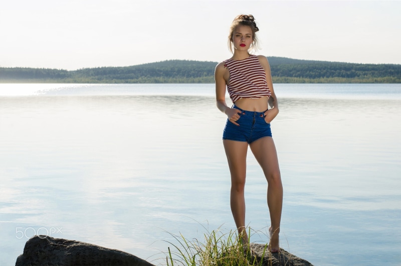sunlight, jean shorts, red lipstick, water, looking at viewer, portrait, 1080P, high waisted short, photography, barefoot, belly, bare shoulders, women outdoors