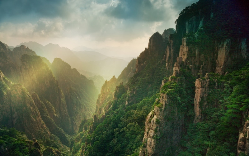 clouds, sky, green color, environment, tree, sun rays, mountain, landmark, outdoors, mountain range, plant, lush foliage, canyon, land, cloud - sky, beauty in nature