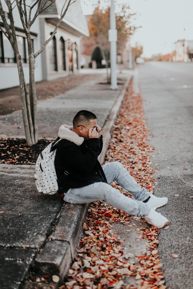 full length, wearing, man, black, beside, day, sitting, leaf, pre-adolescent child, sidewalk, plant part, male, road, white, coat, young adult, real people