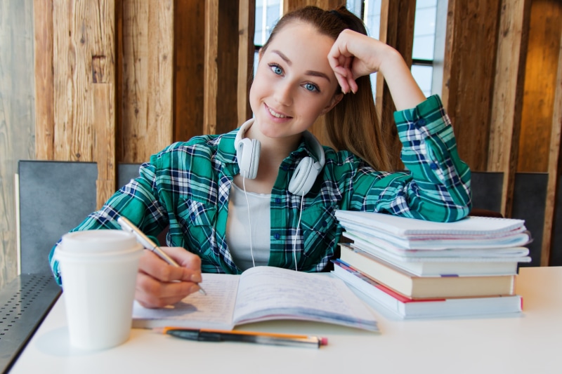 portrait, child, university, education, girl, college, table, indoors, book, headsets, pen, looking at camera, homework, young, hand, head in hands, coffee