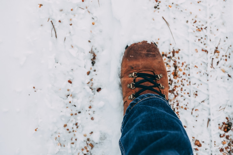 human foot, standing, outdoors, foot, leather, human leg, snow, nature, jeans, one person, brown, body part, covered, person, lifestyles, wearing, directly above