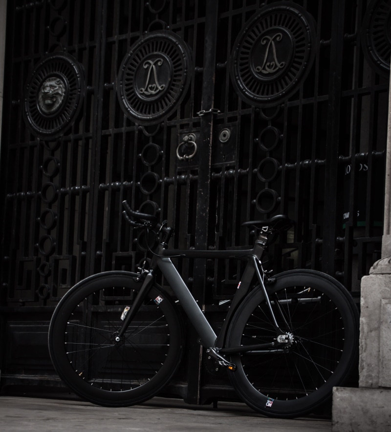 wheel, bicycle, no people, outdoors, road, gear, sidewalk, mode of transportation, gate, black, steel, fixed, land vehicle, building exterior, day, focus on foreground