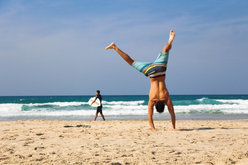 man, handstand, dom, seashore, recreation, person, sportswear, vacation, female, enjoyment, active, land, surfboard, ocean, shape, fun, relaxation, holiday