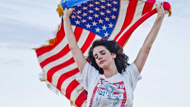 front view, one person, holding, young adult, flag, smiling, adult, patriotism, portrait, lifestyles, women, outdoors, Lana Del Rey, young women, clothing