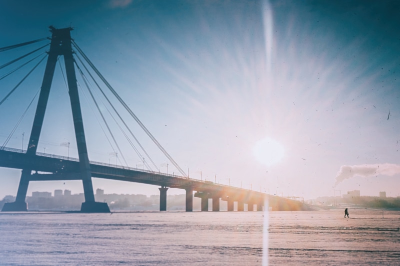 transportation, sun, walking, rise, person, beach, distant, sea, water, tourism, lifestyles, buildings, built structure, connection, sunshine, bridge - man made structure