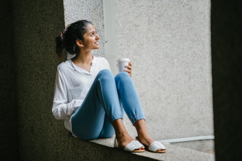 smiling, attractive, drink, young adult, sitting, relaxing, contemplation, coffee cup, break, jeans, side view, fashionable, relaxation, wall, food and drink