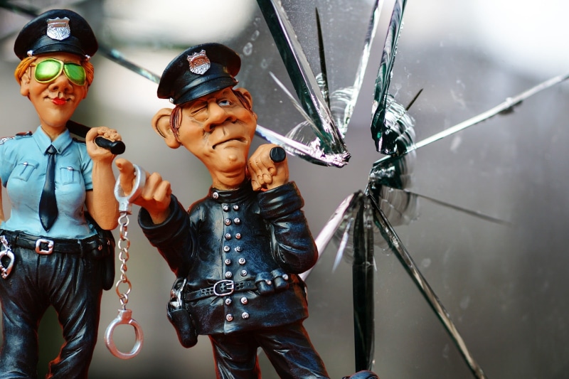 shard, figurines, broken, police car, glass damage, policeman, policewoman, young men, adult, holding, crack, disc, fragmented, window, handcuffs, glasses