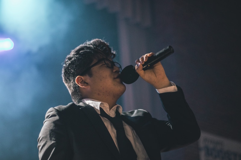 singer, night, adult, microphone, black, music, person, wearing, jacket, event, performer, colors, headshot, suit, stage, man, performance, lights, eyewear