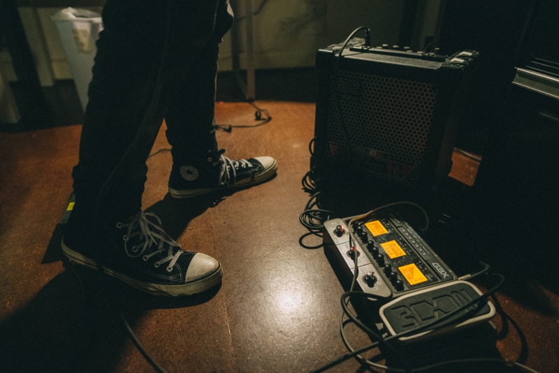 human, cable, amplifier, artist, stage, adult, guitar, human limb, musician, beside, shoes, apparel, music equipment, human leg, man, low section, body part