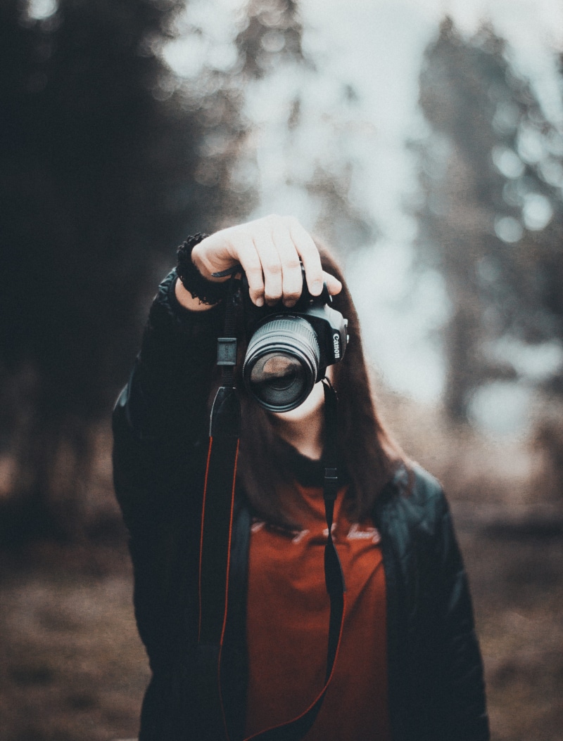 camera - photographic equipment, portrait, holding, hood, one person, focus on foreground, hood - clothing, digital camera, photographic equipment, woman