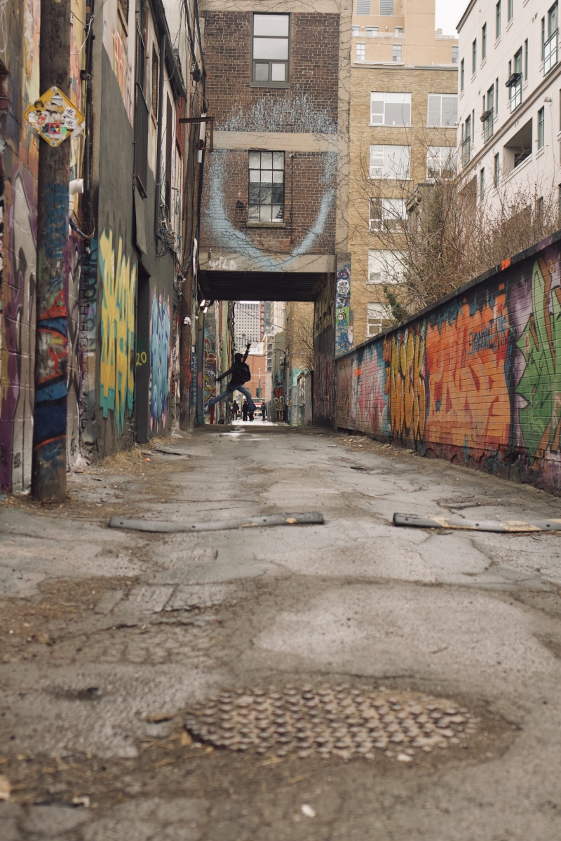 messy, one person, building, brick, direction, person, wall - building feature, can, graffiti, outdoors, residential district, day, road, men, painting
