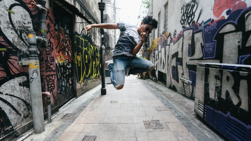 town, young adult, city, wearing, person, outdoors, pants, black, vehicle, apparel, graffiti, architecture, clothing, casual clothing, shirt, man, full length