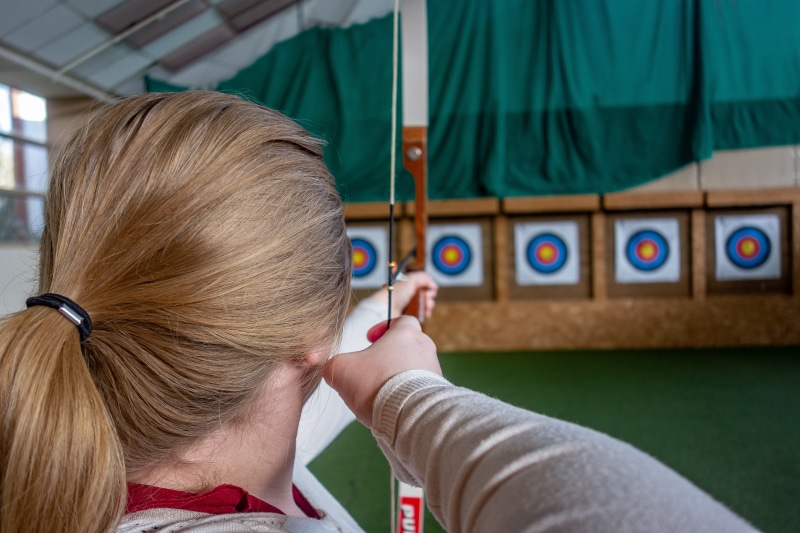 focus on foreground, blond hair, hair, real people, human body part, target, 5K, shooting, one person, lifestyles, arc, females, indoors, room, leisure activity