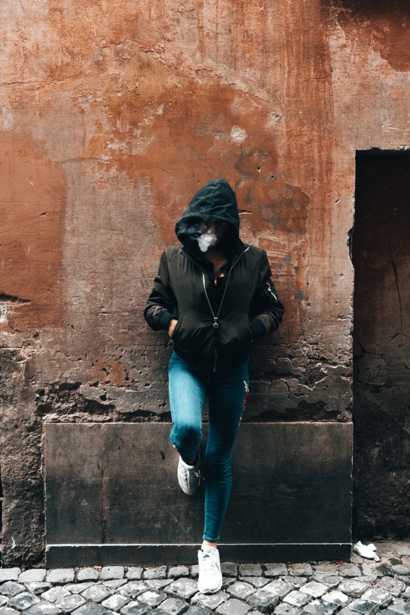 footwear, front view, lifestyles, one person, women, outdoors, girl vaping, edgy, brick, pants, jeans, sweater, casual clothing, leisure activity, clothing