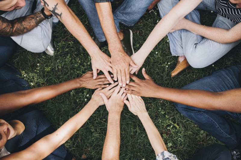 unity, hand stack, togetherness, high angle view, day, sitting, human hand, hand, medium group of people, tattoo, friends, bonding, people, directly above