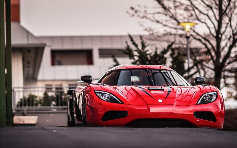 focus on foreground, 1080P, day, land vehicle, outdoors, red, road, nature, city, selective focus, no people, building exterior, transportation, Koenigsegg Agera