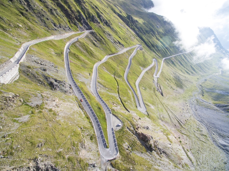 mountain, road, mountain road, green, sunny, outdoors, beauty in nature, fields, grass, non-urban scene, mountain range, cars, gray, sky, nature, concrete