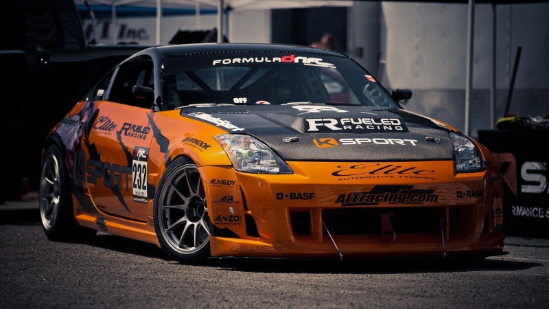 wheel, road, outdoors, day, Nissan 350Z, no people, text, mode of transportation, focus on foreground, 1080P, transportation, street, orange, taxi, orange cars