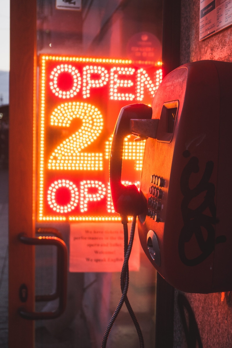 western script, city, outdoors, 5K, close-up, no people, evening, technology, light, led, door, script, pay phone, phone box, orange, urban