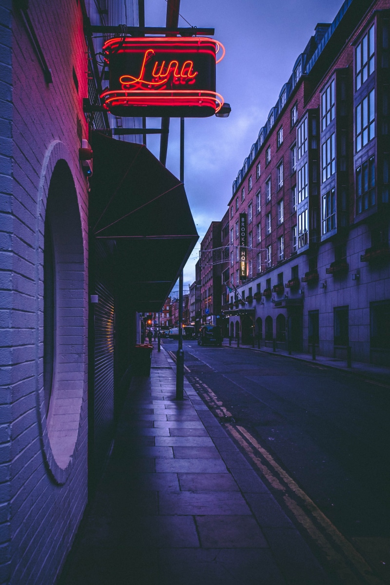 urban, city, incidental people, transportation system, neon, transportation, road, dusk, sign, car, text, buildings, nature, evening, dark, direction, pavement